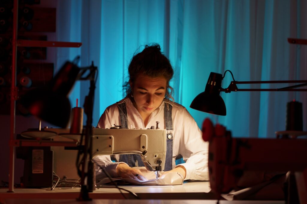 Self-employed young woman work on sewing machine in little creative atelier creating bespoke clothes